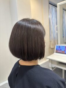 Back view of a person with a sleek dark brown bob haircut seated in a hair salon, facing a mirror.